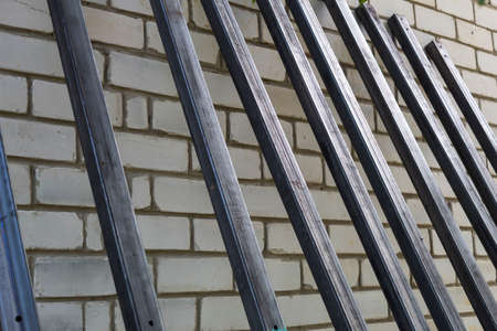 A metal rectangular profile stands against a brick wall.