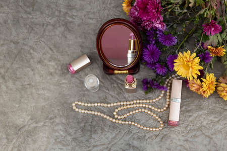 View from above. There is a round mirror on the table, reflecting lipstick, a bottle of perfume, a pearl necklace and autumn flowers.の写真素材