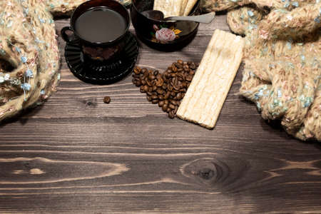 On the table against the background of a warm scarf is a cup of coffee on a saucer, a sugar bowl with a spoon, cookies and coffee beans laid out in the form of a heart.の写真素材