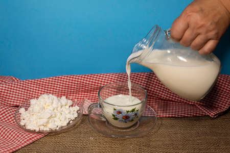 A woman's hand holds a jug of milk, from which it pours into a cup. There is a plate of cottage...