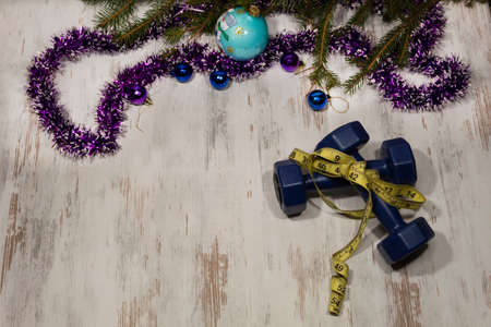 View from above. Dumbbells tied with a centimeter lie on a light background. Next are New Year's tinsel, balls and branches of spruce.の写真素材