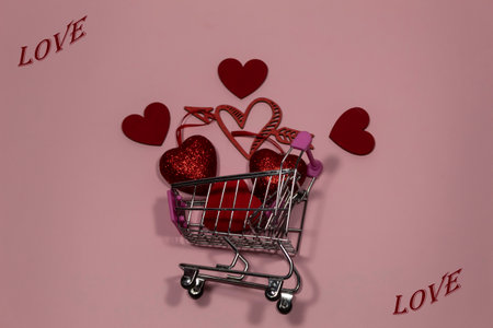 On a pink background, red hearts lie in a supermarket trolley. In the corners the word "Love" is written.の写真素材