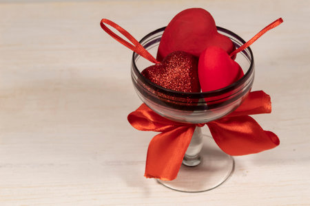 Three bright red hearts lie on a white background in a glass with a red bow.