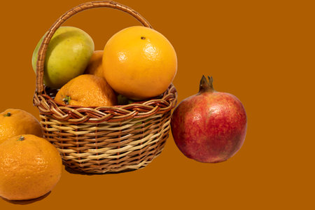 Isolate on a brown background. The basket contains green apples, oranges and tangerines. There are pomegranates and tangerines nearby.の写真素材