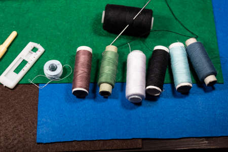 On the table are multicolored threads, a needle, a spool of thread, and pieces of felt fabric.の写真素材