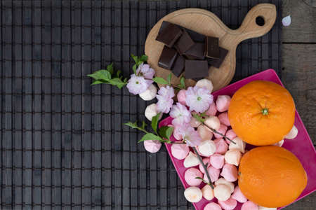 On the table is a cutting board with pieces of dark chocolate, there is a dish with oranges and...