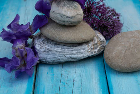 A pyramid of flat stones stands on a blue background. Nearby lie blue iris flowers and decorative onions.の写真素材