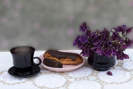 On a blurred gray background, there is a cup of coffee on a napkin. On a pink saucer is a cake and...