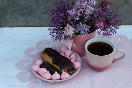 There is a cup of coffee on a pink napkin, a cake and sweets on a saucer. There is a pink bucket of...