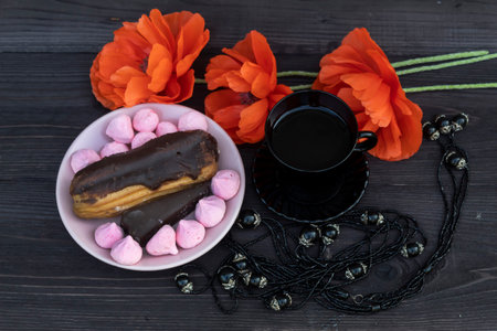 View from above. On a dark wooden background, there is a black cup of coffee and a dark necklace....