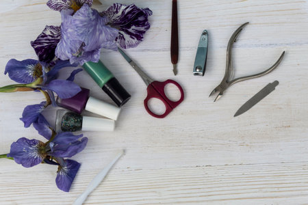 Three irises, nail polish and manicure instruments lie on a white wooden background.