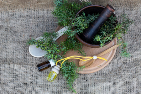 On the jute cloth lies a cutting board, a wooden spoon, bottles of oil, juniper branches with berries, and a bowl.の写真素材