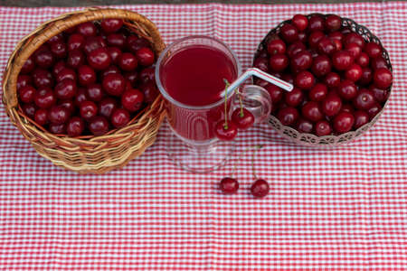 View from above. There is a glass of cherry compote with a straw on a checkered napkin. Nearby, in a...