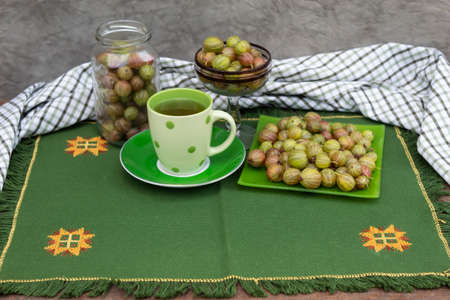 On a green napkin a saucer, a jar and a bowl with gooseberries. In the center is a cup of gooseberry drink.の写真素材