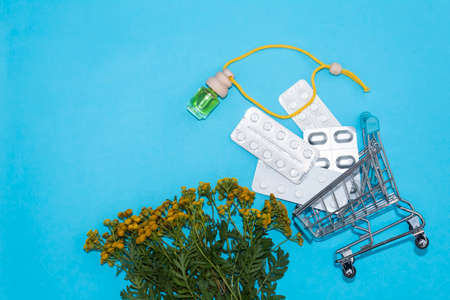 On a blue background, a trolley with plates of tablets. Nearby lies the medicinal herb tansy and a...