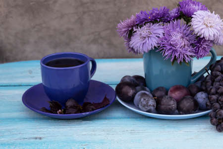 There is a cup of tea, a bouquet of asters on the table, and plums on a saucer.の写真素材