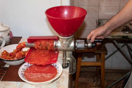A man in the kitchen turns a mechanical juicer to prepare tomato juice.