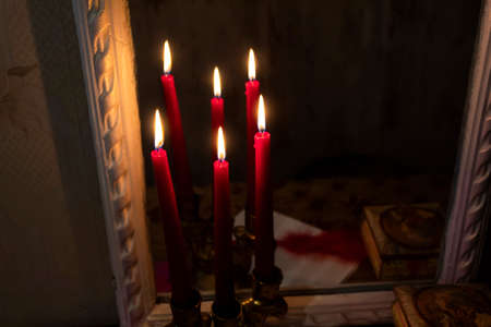Three lighted red candles stand in the dark near the mirror, reflecting in it.の写真素材