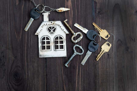 A mock-up of a house and seven different keys lie on a dark wooden background.の写真素材