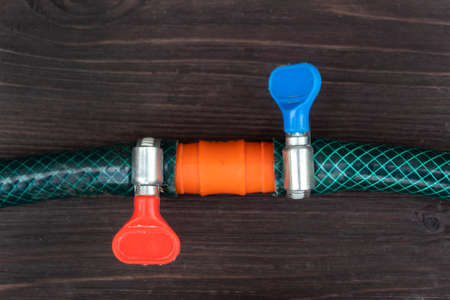 On a dark wooden background lies a watering hose connected by a sleeve and a clip.の写真素材