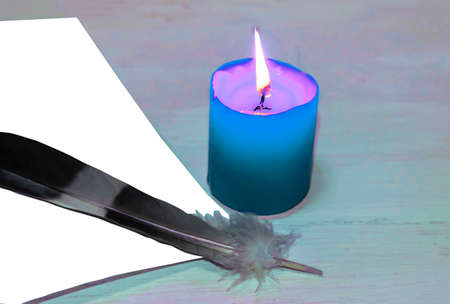 There is a burning blue candle on the table, a white sheet of paper and a quill.の写真素材