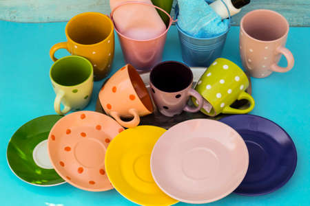Against a blue background, there are multi-colored dishes - saucers and cups and two buckets of napkins.の写真素材