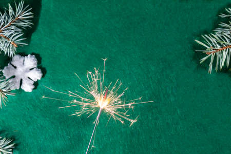 Christmas background. Snowflake and spruce branches lie on a green background. There is a sparkler...