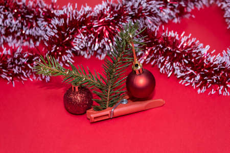 On a red background, a small spruce branch is held by a red clothespin. There are two Christmas balls hanging on a branch. Behind the tinsel.の写真素材
