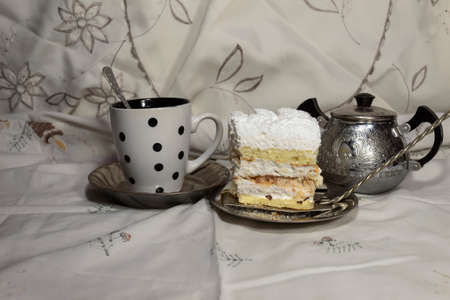 Still life. There is a cup of tea on the table, a piece of cake on a saucer. There is a sugar bowl...