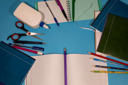 Notebooks, pens, pencils, glue, scissors, notepads lie on a blue background.