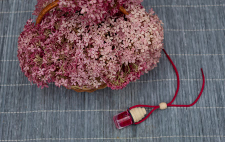 On a bamboo napkin lies a bottle of rose oil and a basket of pink flowers.
