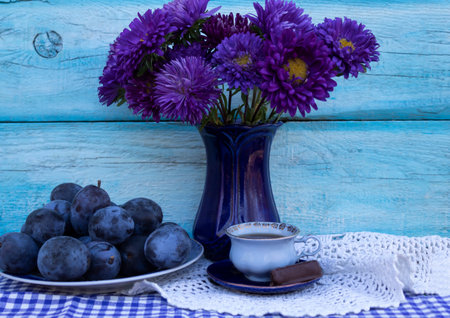 Blue plums, a bouquet of blue asters and a cup of coffee with candy.の写真素材