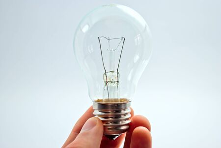 His fingers hold a light bulb on a light background.