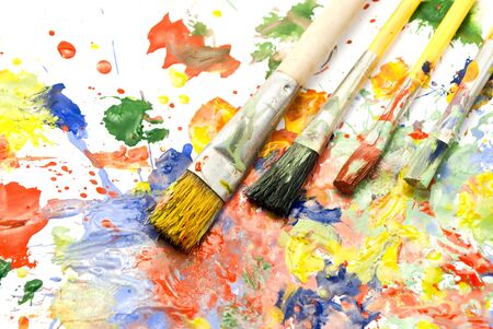 Different sizes paintbrushes against a background of multicolored paint spread.