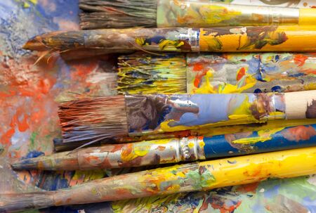 Different sizes paintbrushes against a background of multicolored paint spread.の写真素材