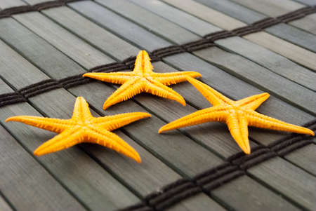 Three orange seastars on a wooden mat.