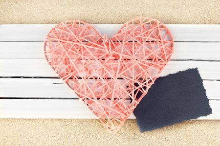 Pink wicker heart on a wooden planks over sandy background.の写真素材