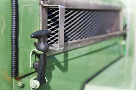 Hood holder made of black rubber on the side of an old green tractor.