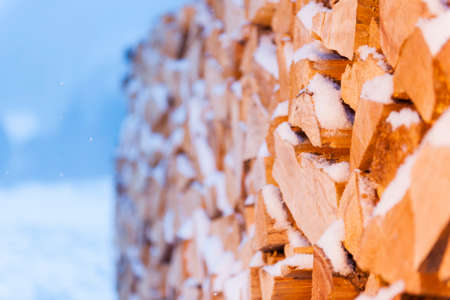 Full-sized side view of freshly beaten, stacked and snow-covered firewood in front of evening...