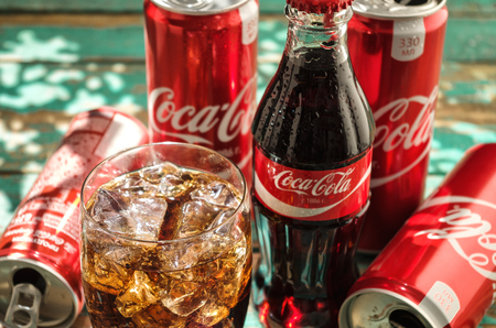 MINSK, BELARUS-AUGUST 26, 2016: Glass of Coca-Cola with ice, can and bottle of Coca-Cola on wooden background. Coca-Cola is a carbonated soft drink sold in stores, throughout the world.のeditorial素材