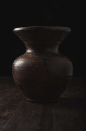 Dark clay vase with highlights on dark wooden backgroundの写真素材