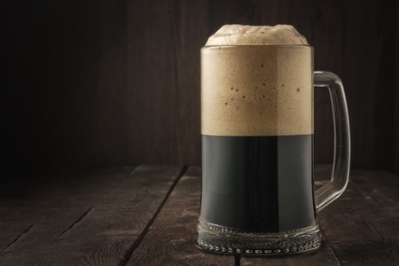 Dark beer mug with foam on dark wooden background