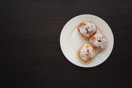 Tradition Jewish holiday sweets, donut sufganiyot with sugar powder and jam on dark wood background...