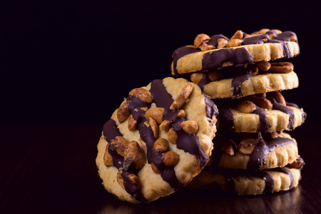 Cookies with peanuts, covered with chocolate icing, on a dark wooden background with space for textの写真素材