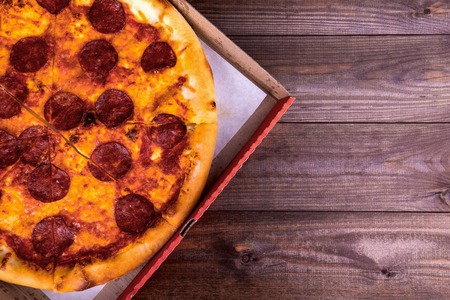 Pizza with salami in a box on a wooden background with copy space. Top viewの写真素材