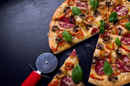 Hot and delicious pizza with salami tomatoes cheese and mushrooms ready to eat on a black wooden background. Top viewの写真素材
