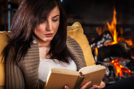 Young woman reading a book by fireplaceの写真素材