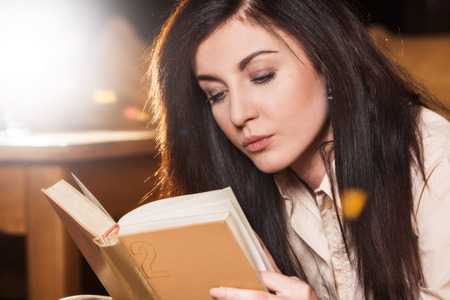 Young woman lying on her couch reading a book at home in the sitting roomの写真素材