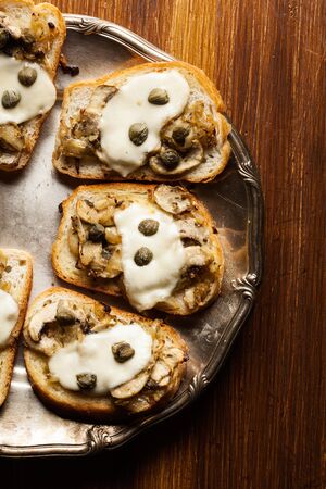 Crostini with fried mushrooms, onion and mozzarella cheese on a plateの写真素材
