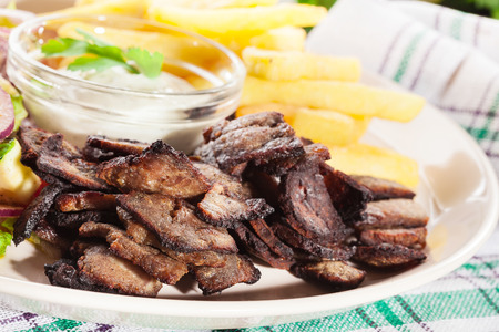 Grilled meat with French fries and fresh vegetables on a plateの写真素材